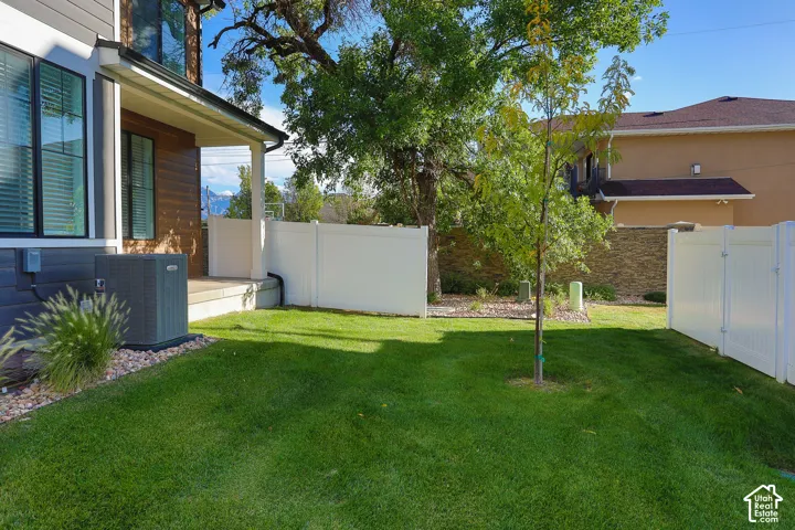Expansive grassy area with a young tree, bordered by white privacy fencing and a stone retaining wall