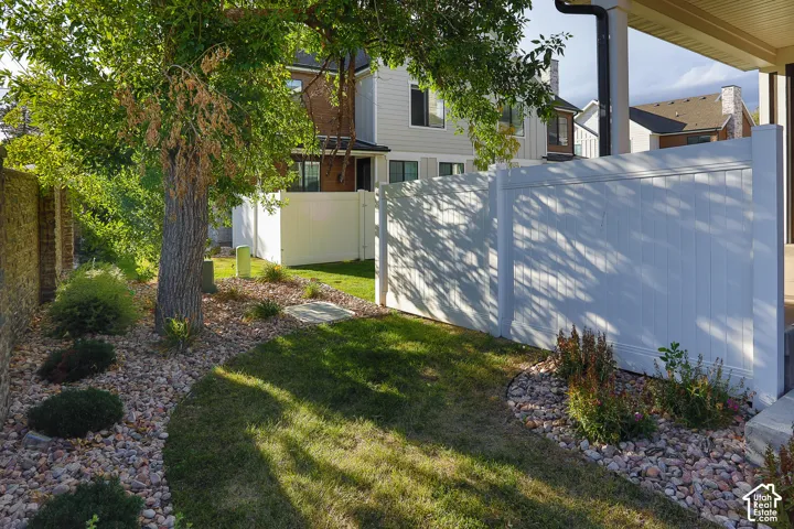 Manicured landscape featuring a mature tree, mixed stone and grass ground cover, and a white privacy fence