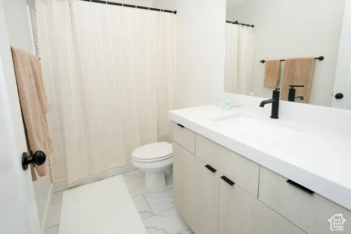 White integrated sink with a matte black faucet, light wood-finish vanity with black hardware, full-width mirror, and white tile flooring