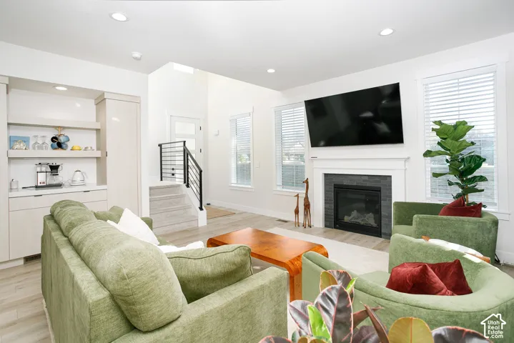 Living area with wood-finish flooring, a built-in beverage station, a fireplace with a dark tile surround, and multiple windows with blinds