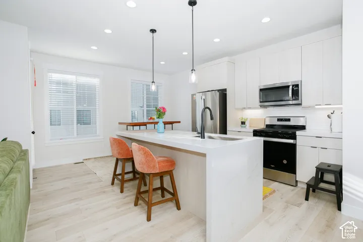 Bright kitchen featuring a waterfall island, stainless steel appliances, white cabinetry, wood-finish flooring, and recessed lighting