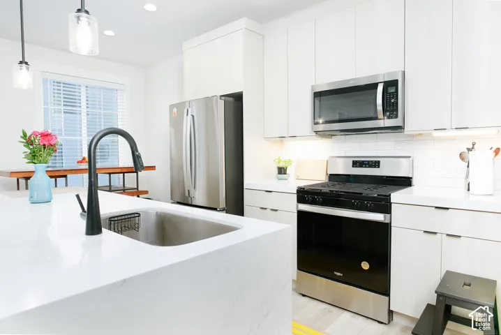 Kitchen featuring white cabinetry, stainless steel appliances, white countertops, a single basin sink with a black gooseneck faucet, and white subway tile backsplash