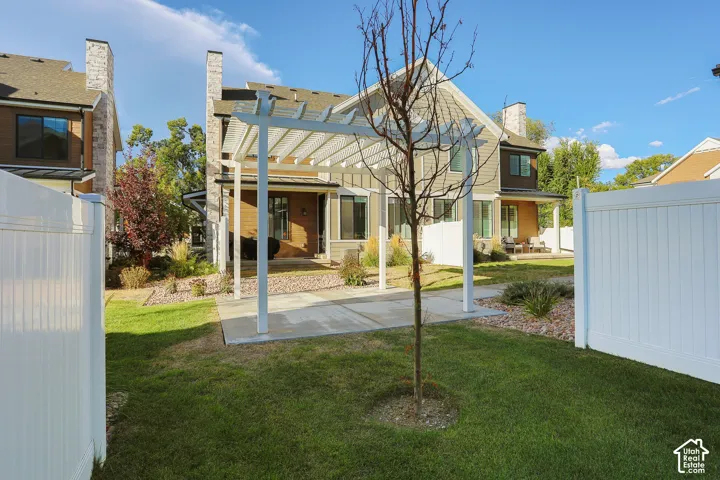 Expansive lawn area with a white privacy fence, concrete patio, and a white pergola