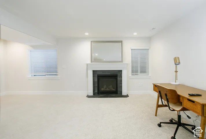 Recessed lighting, fireplace with a tile surround, white mantel, two windows with horizontal blinds, and neutral carpet flooring