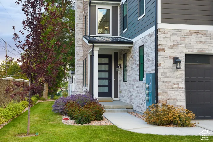 Stone veneer exterior with dark siding accents, a modern entry door with vertical glass panels, a covered entry porch, and a dark garage door