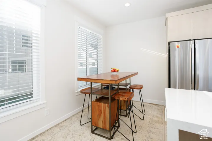 Stainless steel refrigerator, white quartz countertop, light wood-finish cabinetry, recessed ceiling lighting, and white window blinds