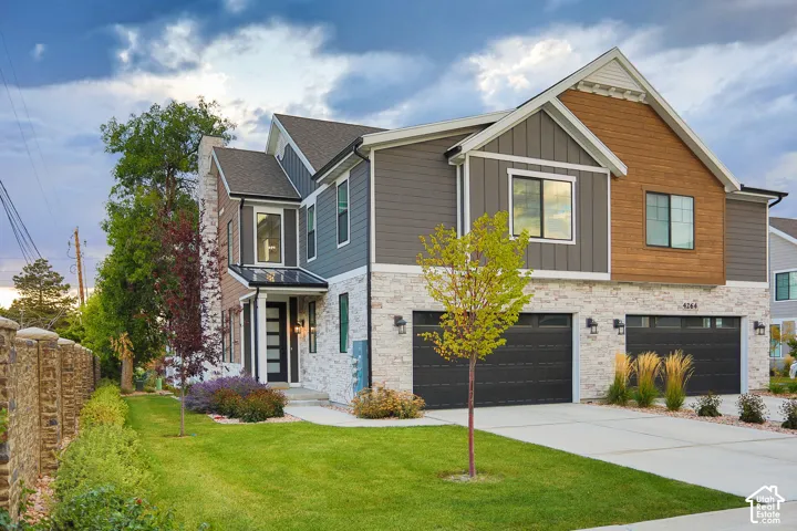 Contemporary exterior featuring mixed material siding, dual garages with black doors, a prominent front entry, and a manicured lawn
