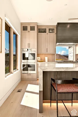 Integrated stainless steel appliances, light wood-finish cabinetry, a waterfall island with stone countertop, and light wood-finish flooring