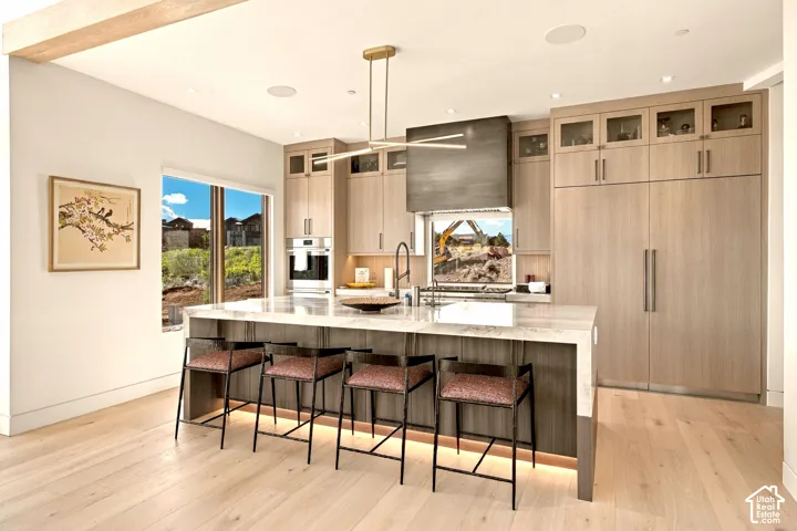 Gourmet kitchen featuring a large central island with integrated lighting, wood-finish cabinetry, built-in appliances, and light wood-finish flooring