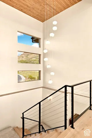 Wood-finish ceiling with a multi-light pendant fixture, linear windows, cable rail staircase, and hardwood flooring