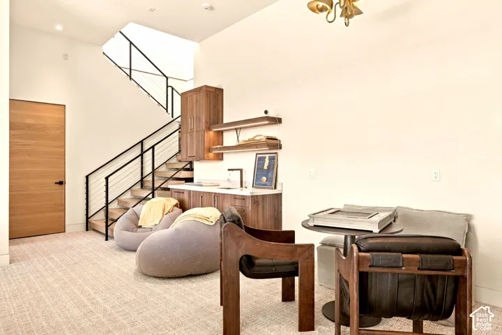 Hardwood staircase with black metal railing, built-in cabinetry with integrated lighting, wood-finish door, and patterned carpet flooring