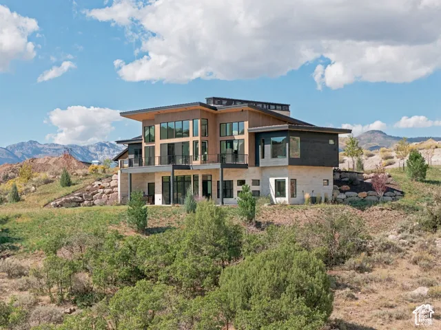 Modern architectural design with extensive window walls, multiple balconies, a flat roof, stone facade accents, and surrounding natural landscape
