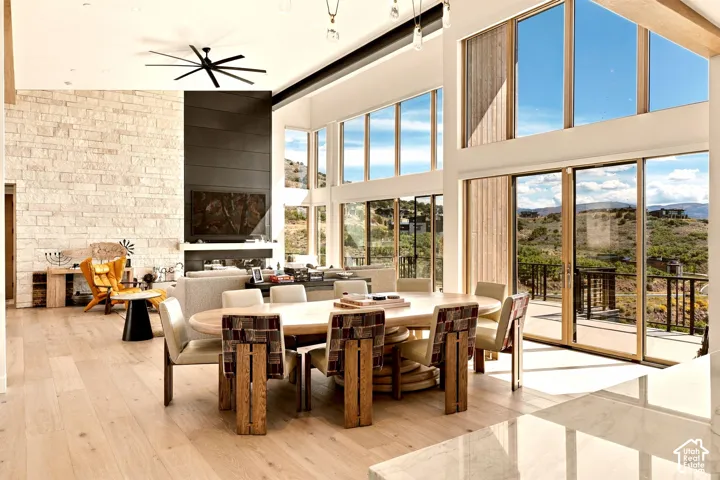 Expansive living area featuring soaring ceilings, a stone accent wall, wood-finish flooring, a contemporary ceiling fan, and large windows with integrated sliding glass doors leading to an outdoor deck