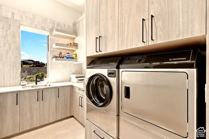 Integrated laundry appliances, light wood-finish cabinetry, sleek black hardware, white countertop, and tiled backsplash