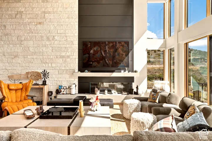 Floor-to-ceiling windows, stone-clad fireplace wall, integrated linear fireplace, light wood-finish flooring, and a modern built-in entertainment center