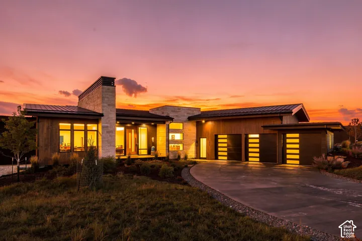 Contemporary exterior featuring stone and wood-finish siding, multiple garage doors with frosted glass panels, a concrete driveway, and integrated landscaping
