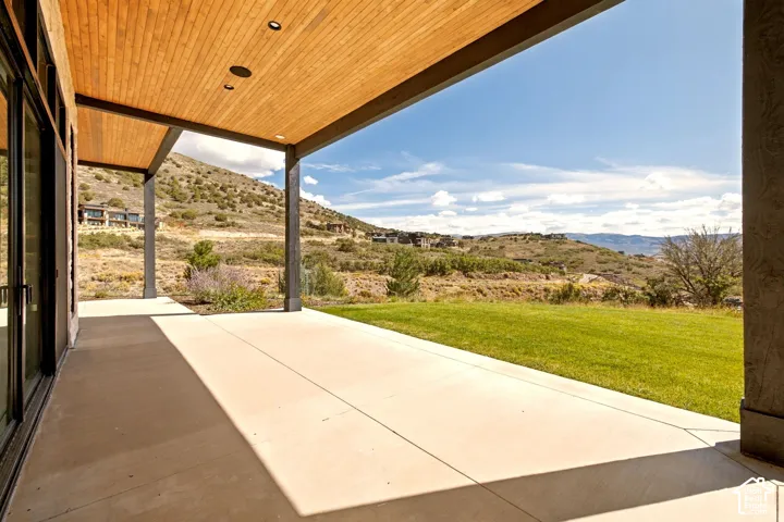 Expansive concrete patio with a wood-finish ceiling, integrated lighting, and a manicured lawn