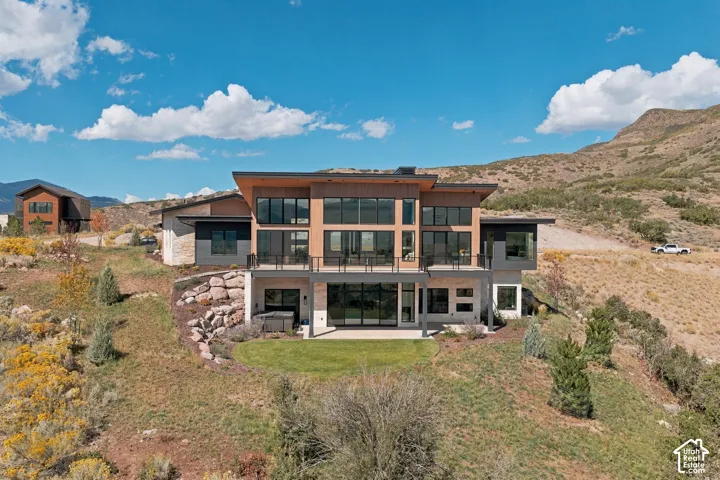 Modern architectural design featuring expansive glass, multiple balconies, a lower-level patio, and a manicured lawn