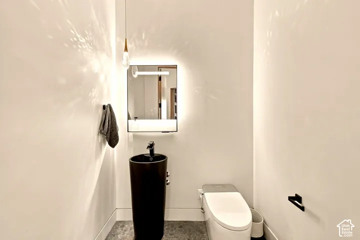 Pedestal sink with a matte black faucet, illuminated vanity mirror, and mosaic tile flooring