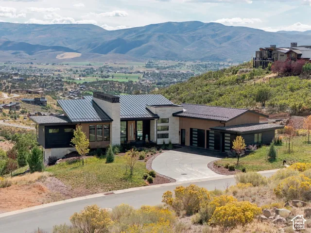 Modern residence featuring a metal roof, stone and wood-finish exterior, large windows, and a paved circular driveway