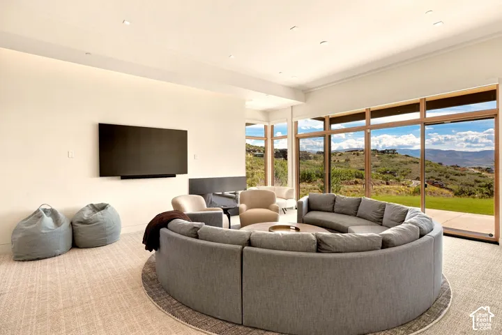 Recessed lighting illuminates the open living space featuring a wall-mounted media console, a built-in fireplace, and expansive floor-to-ceiling windows with wood-finish frames
