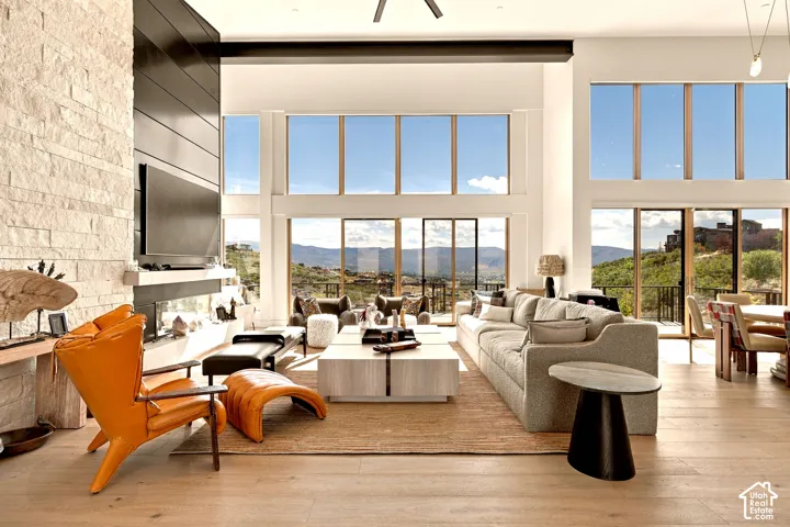 Spacious living area featuring high ceilings, wood-finish flooring, an integrated linear fireplace with a stone-clad surround, and large windows with sliding glass doors