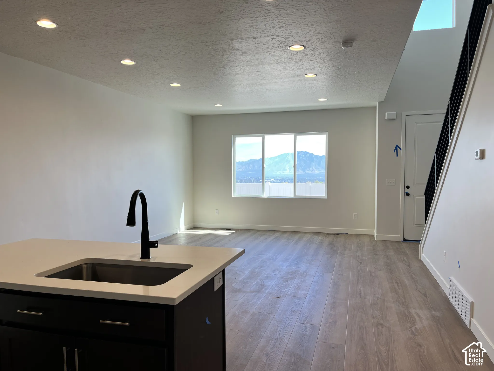 Recessed ceiling lighting, wood-finish flooring, island with integrated sink, black cabinet hardware, and mountain scenery