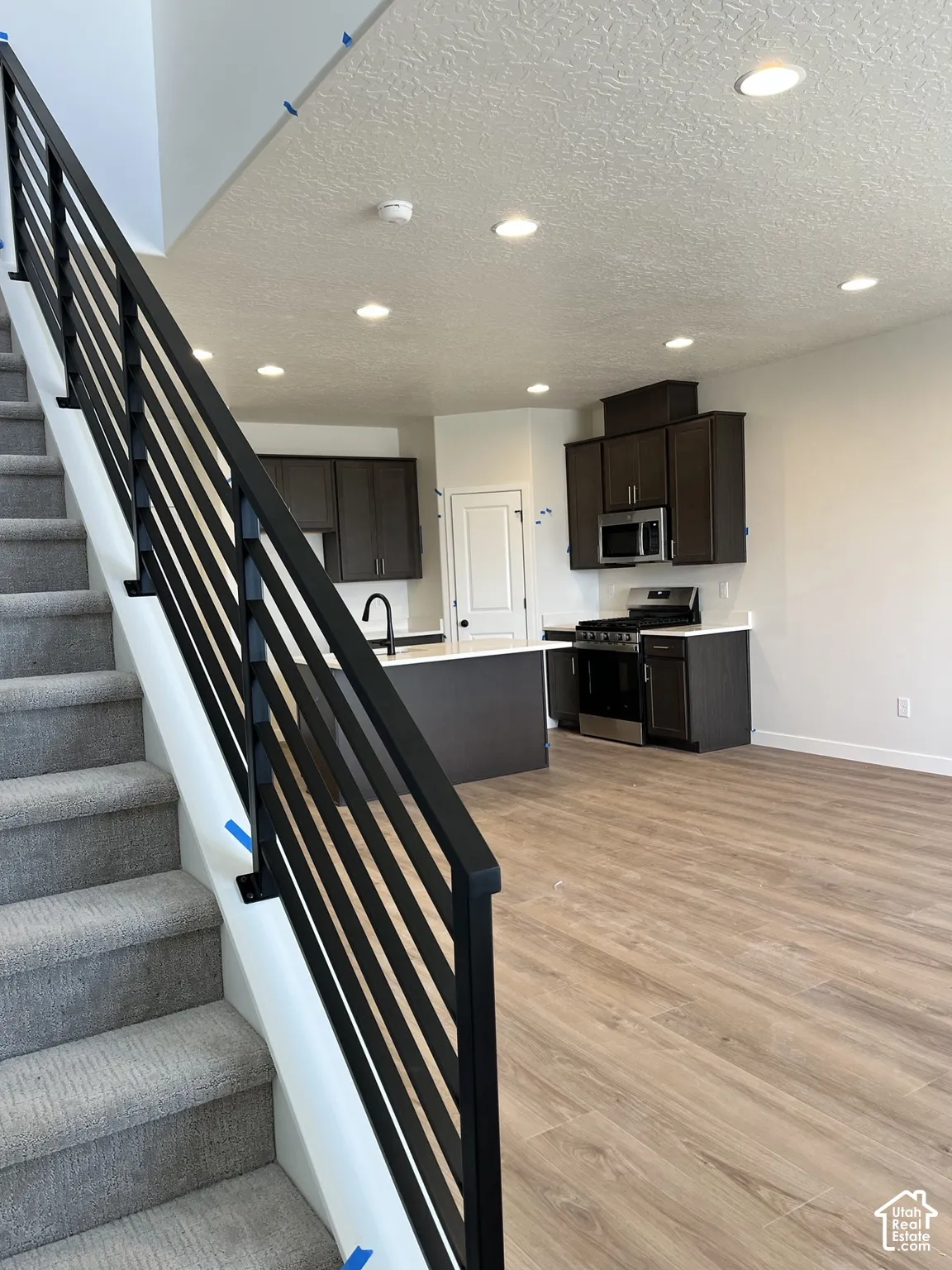 Open-concept living space with wood-finish flooring, a contemporary kitchen featuring dark cabinetry, and an island with white countertops