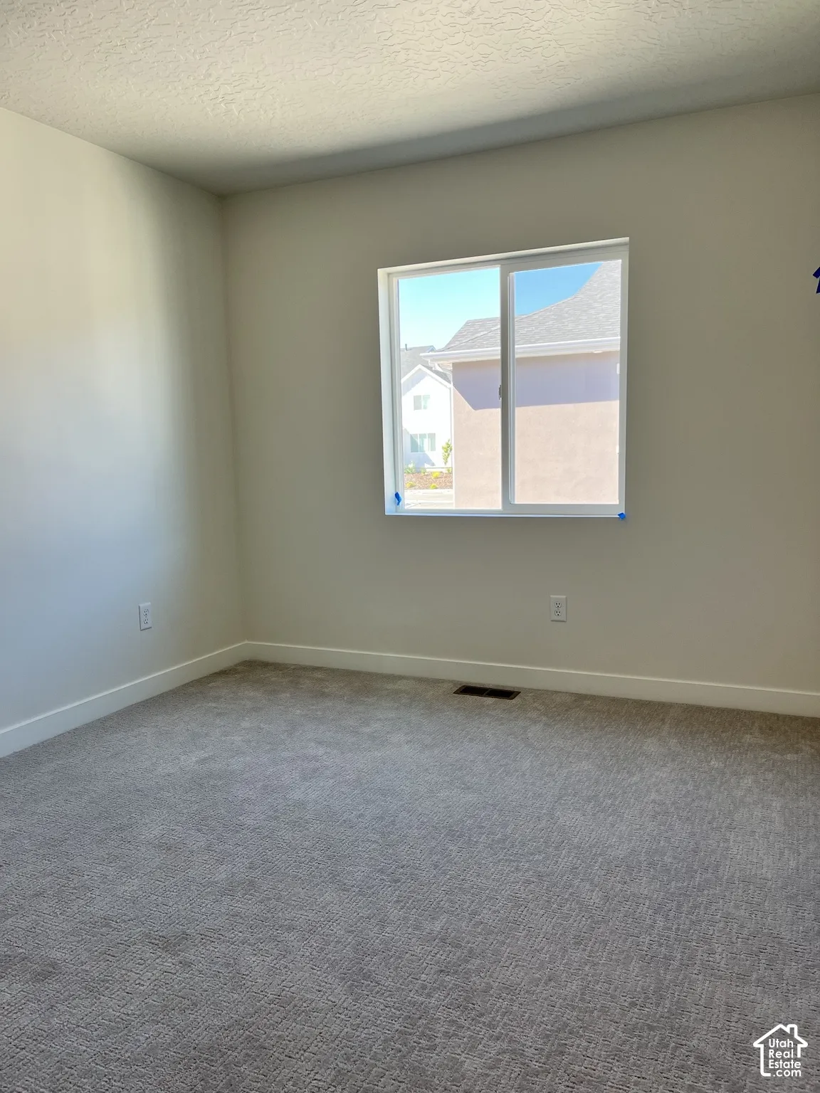 Neutral tone wall paint, textured ceiling, light gray carpeting, and a white framed window