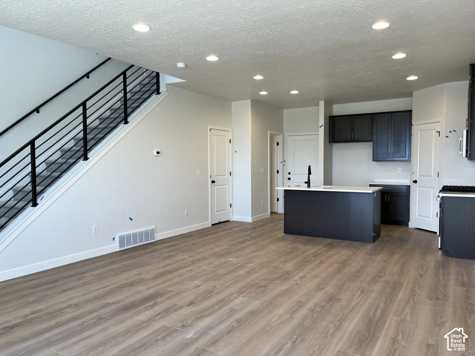 Open-concept living space with wood-finish flooring, recessed lighting, and a modern staircase featuring black metal railings
