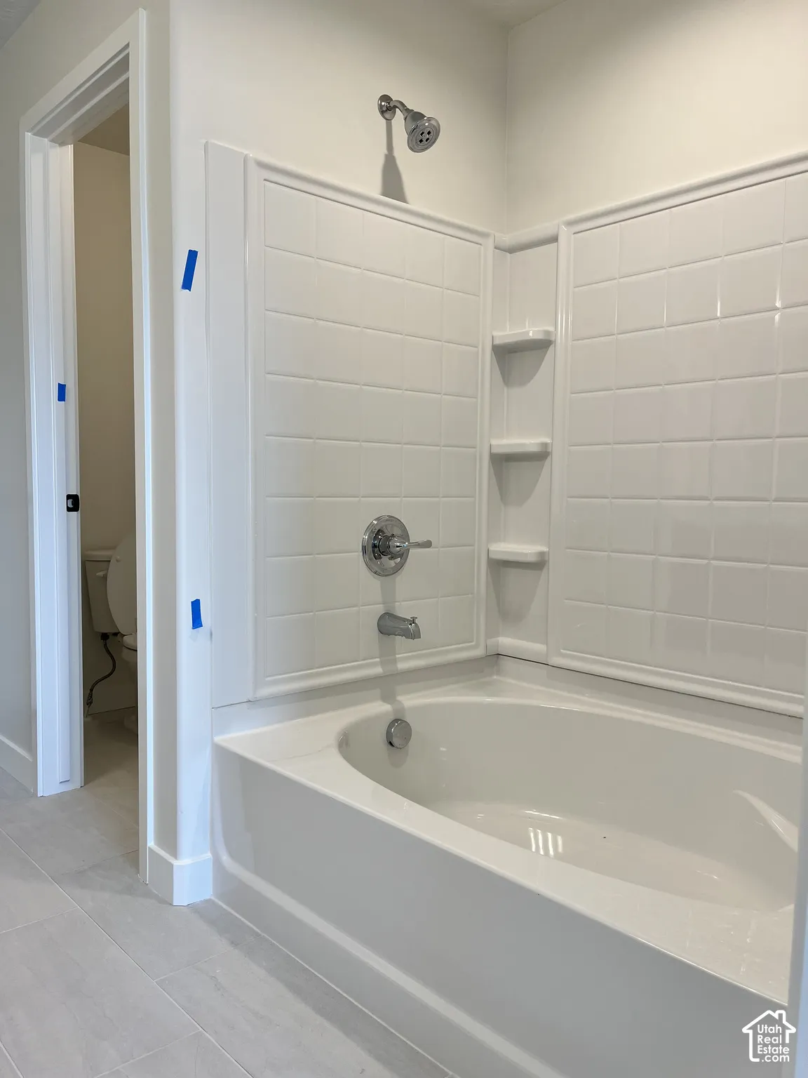Bathtub with integrated shelving, chrome fixtures, and tiled surround