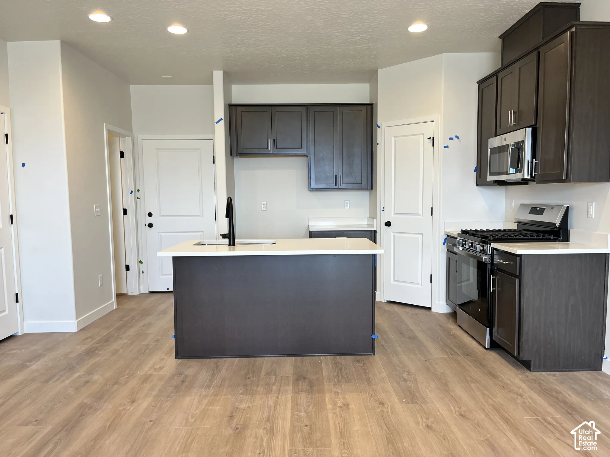Open-concept kitchen with wood-finish flooring, dark wood cabinetry, white countertops, and stainless steel appliances