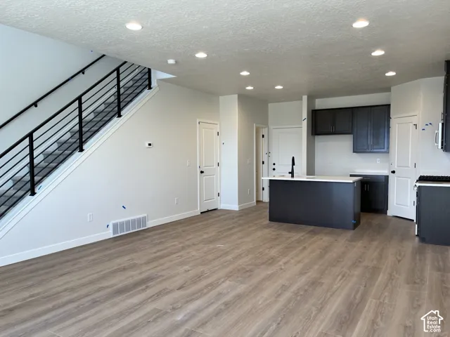 Open-concept living space with wood-finish flooring, recessed lighting, and a modern staircase featuring black metal railings