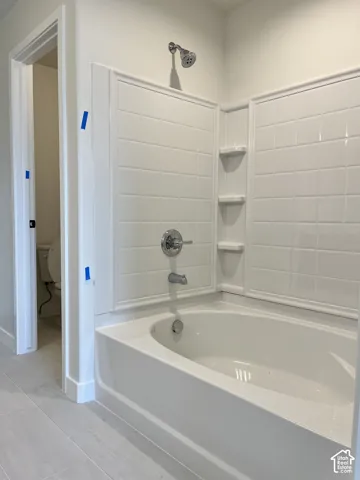 Bathtub with integrated shelving, chrome fixtures, and tiled surround