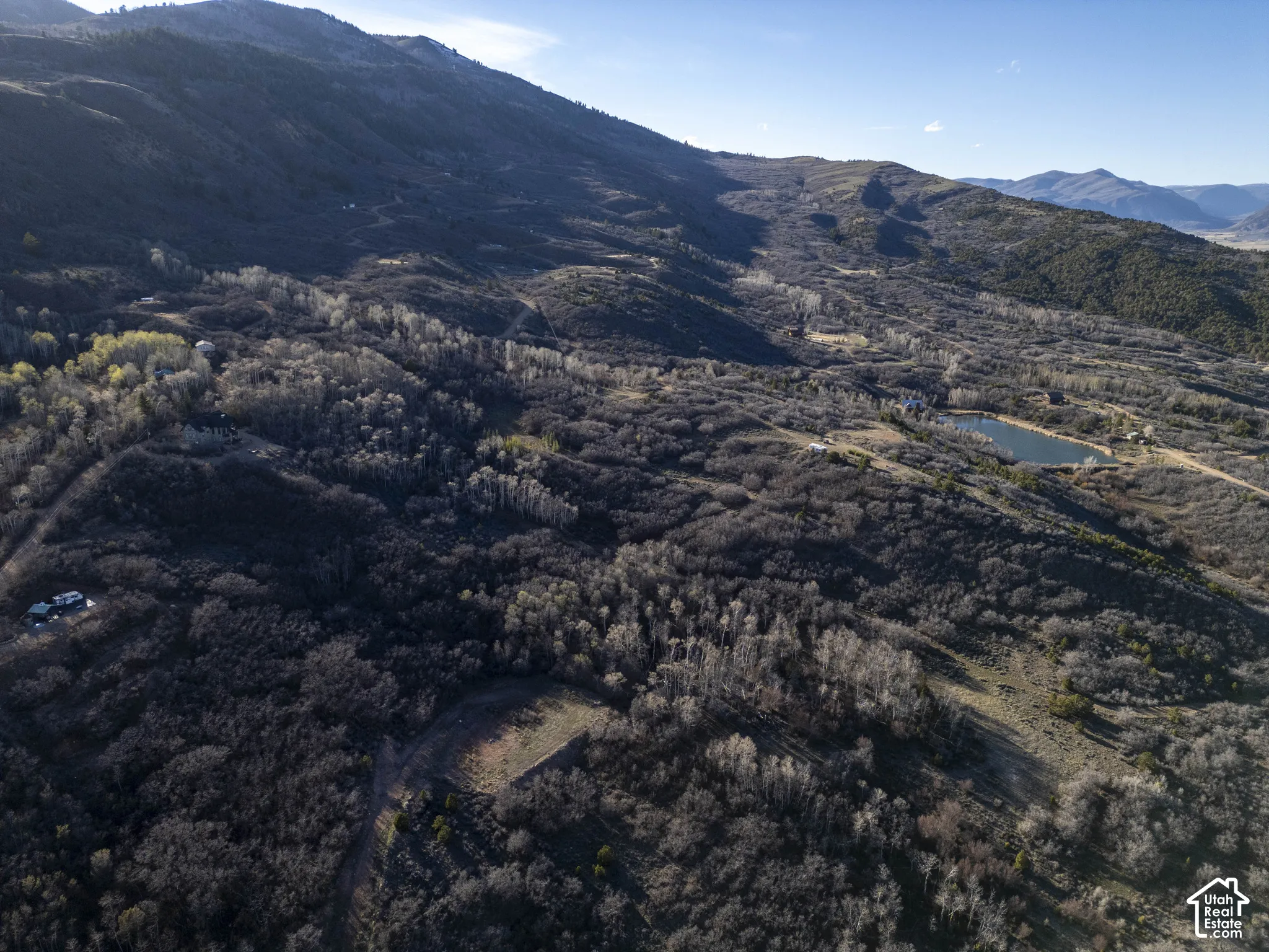 Expansive mountainous terrain featuring diverse tree coverage, a prominent body of water, and distant mountain backdrops