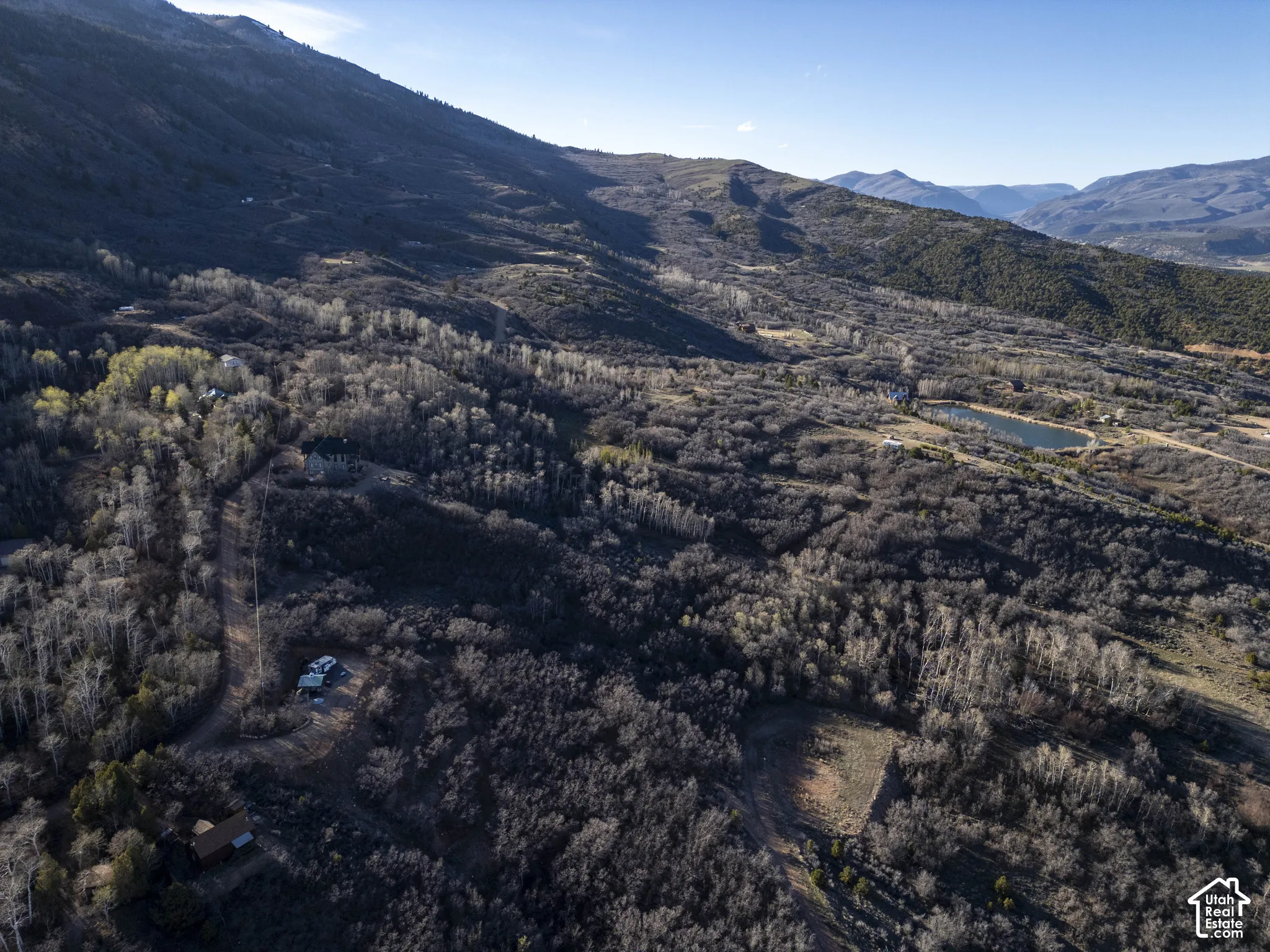 Expansive mountainous terrain featuring dense forests, a distant body of water, and natural clearings
