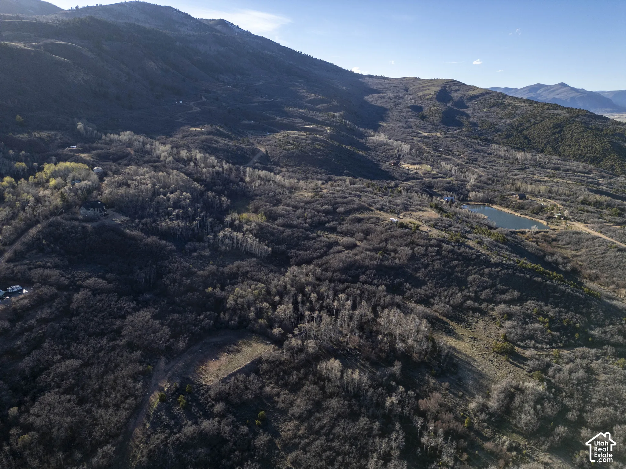 Expansive mountainous terrain featuring a prominent body of water, a winding unpaved road, and diverse tree coverage