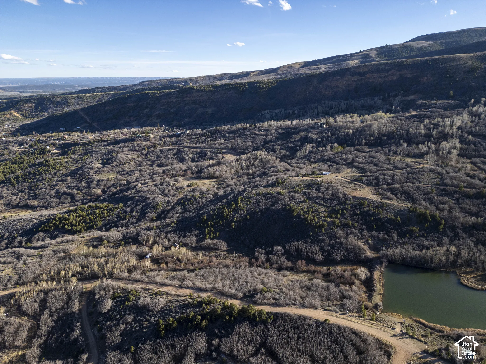 Expansive mountainous terrain featuring varied tree cover, a natural pond, and distant structures