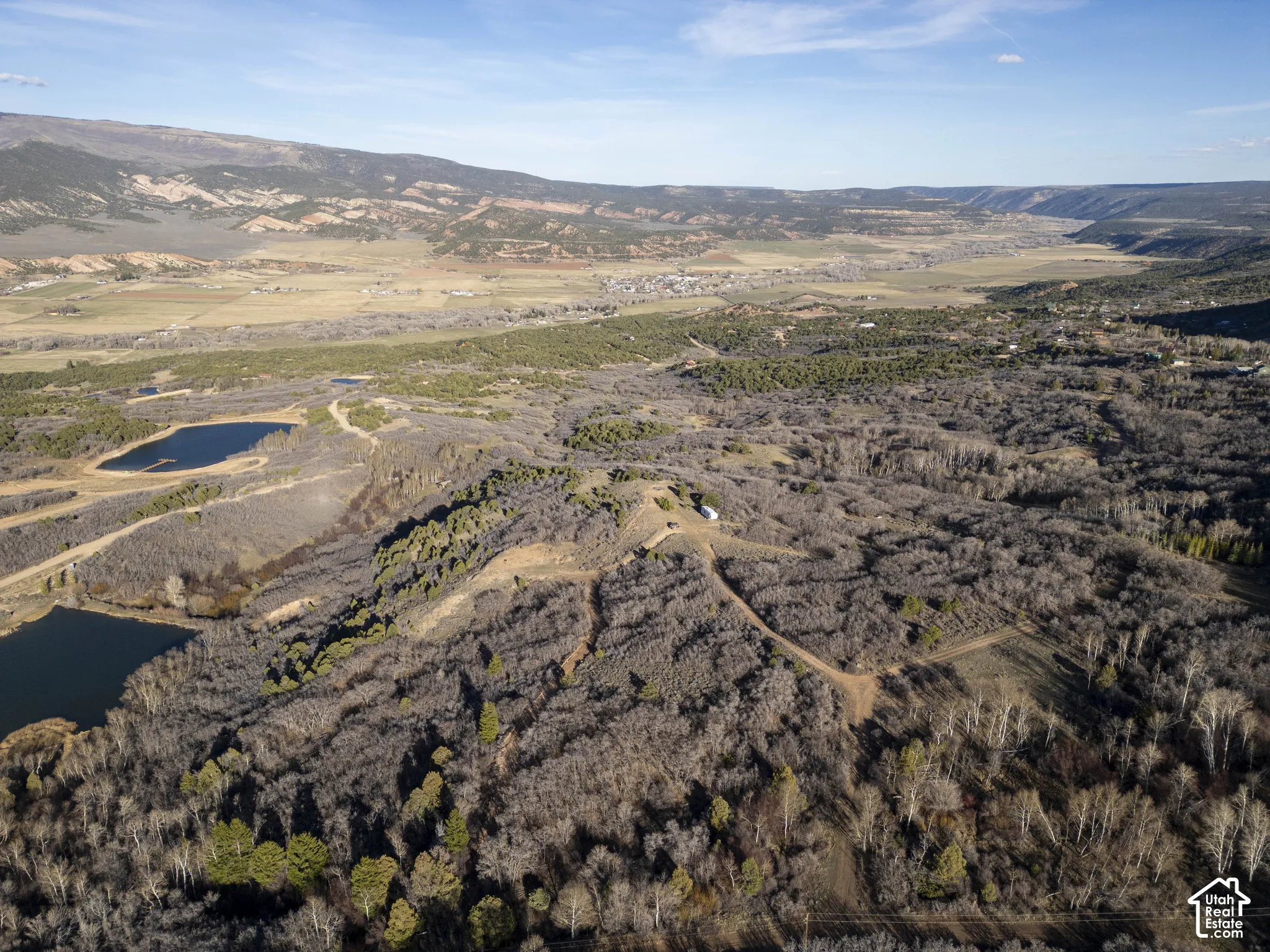 Expansive natural landscape featuring two prominent ponds, varied tree cover, and distant mountain ranges