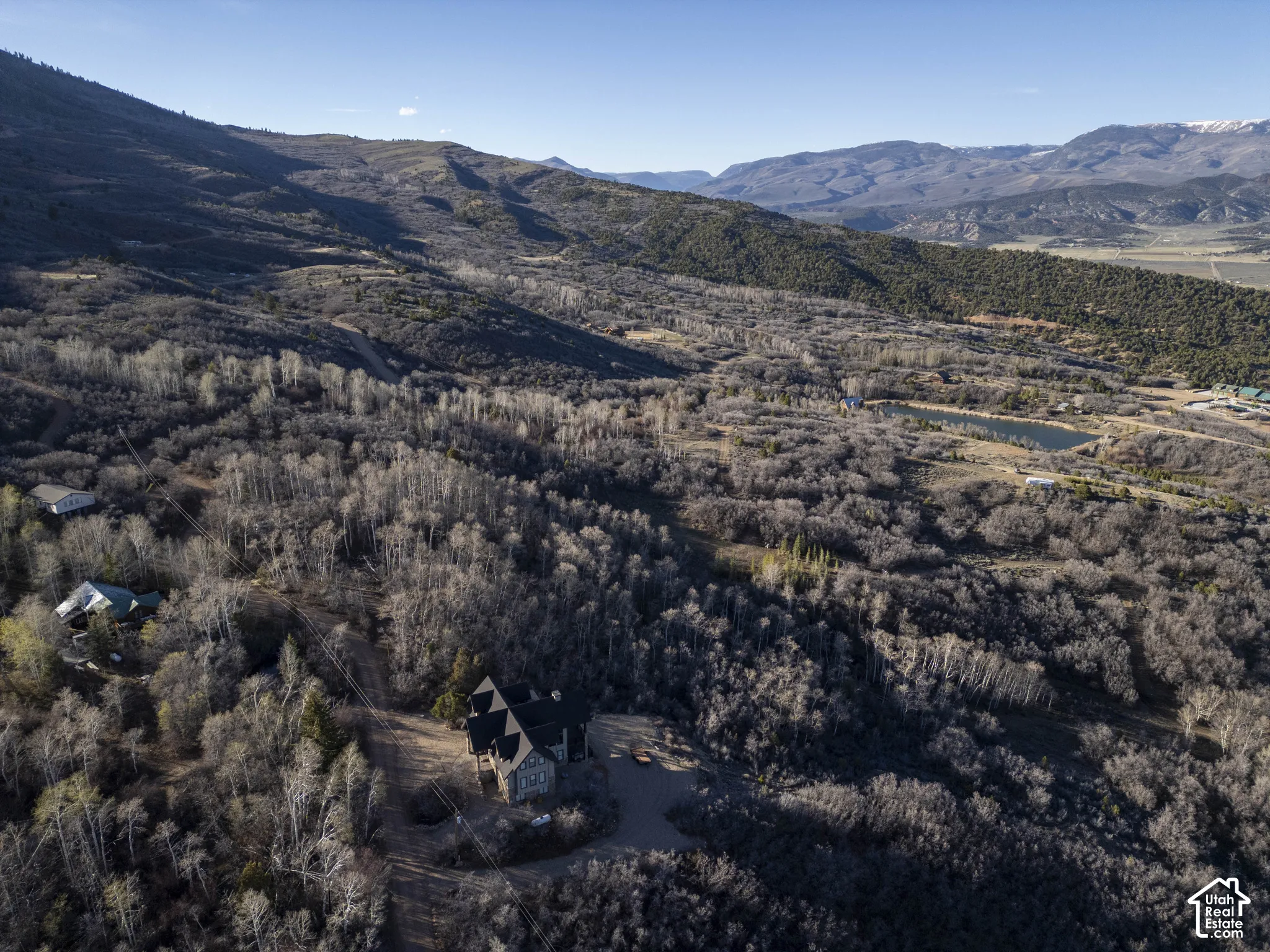 Expansive property featuring a stone and wood-sided structure, surrounded by mature trees, with distant mountains and a pond visible in the landscape