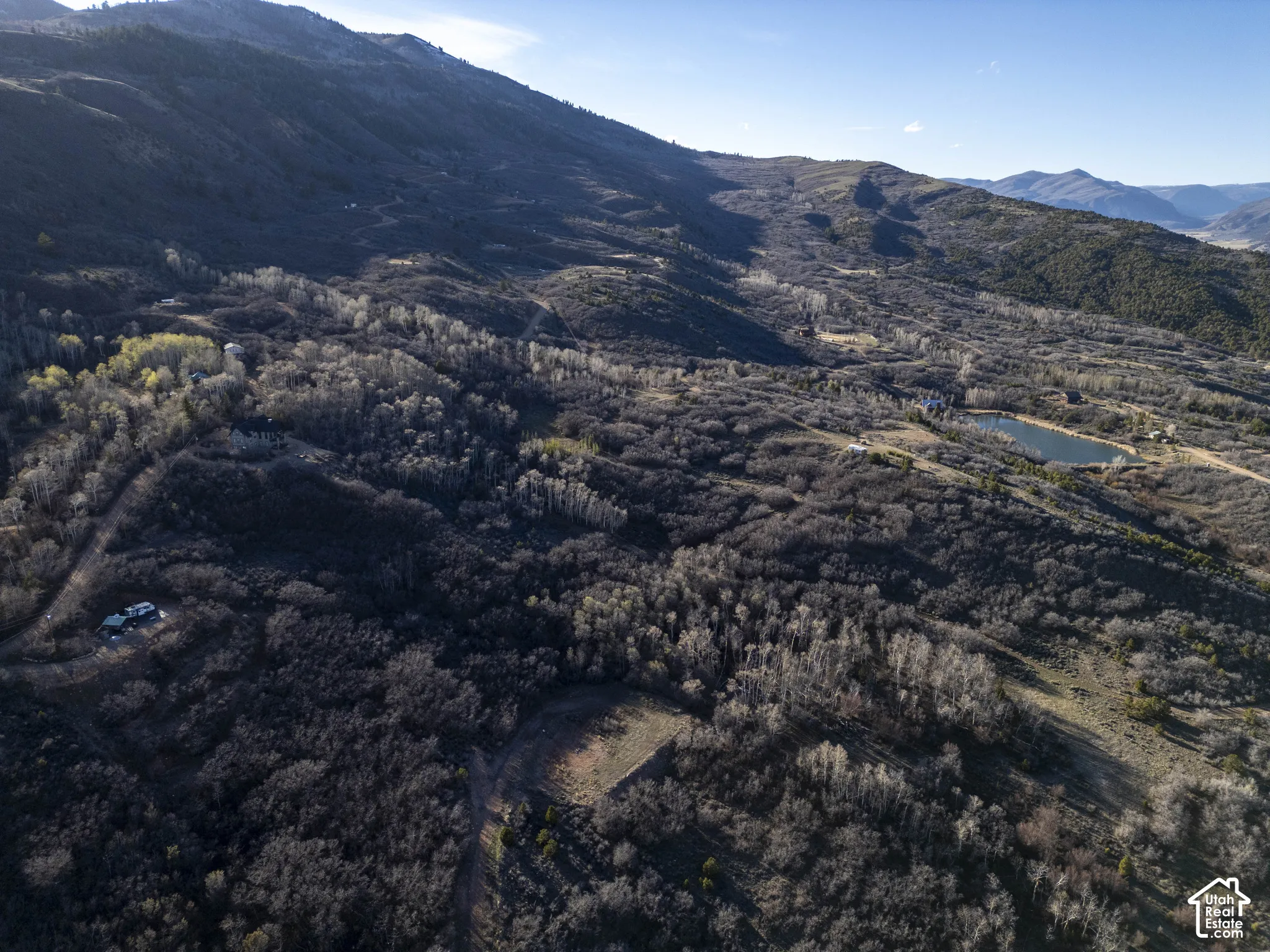 Mountainous landscape with expansive undeveloped terrain, a natural pond, scattered trees, and distant structures