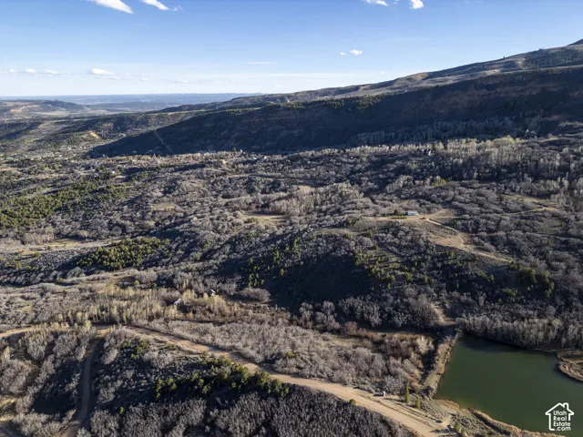Expansive natural landscape with varied tree coverage, a natural body of water, and distant mountain ranges