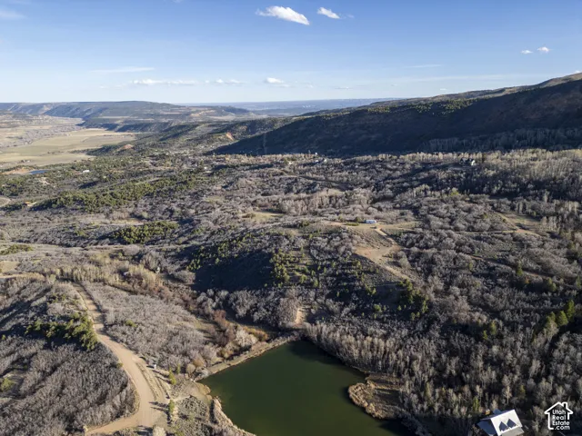 Expansive natural landscape featuring varied terrain, a visible body of water, and distant mountain ranges