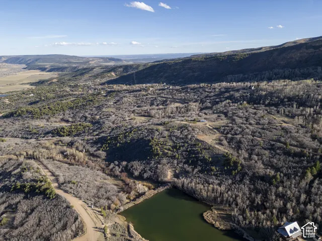 Expansive natural landscape featuring rolling hills, a large body of water, and distant mountain ranges