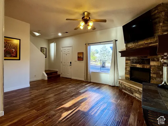 Wood flooring throughout, featuring a stone-clad fireplace with a dark wood mantel, and an overhead ceiling fan with integrated lighting