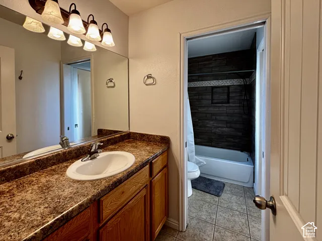 Vanity with integrated sink and countertop, wood-finish cabinetry, and a multi-bulb light fixture