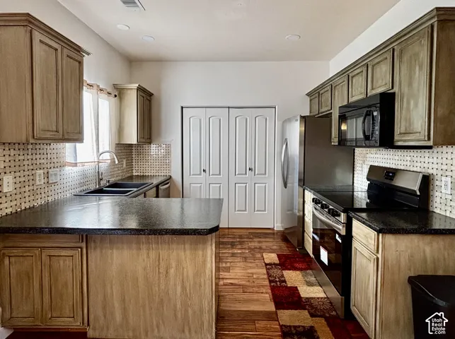 Kitchen featuring wood-finish cabinetry, dark countertops, a mosaic tile backsplash, and stainless steel appliances