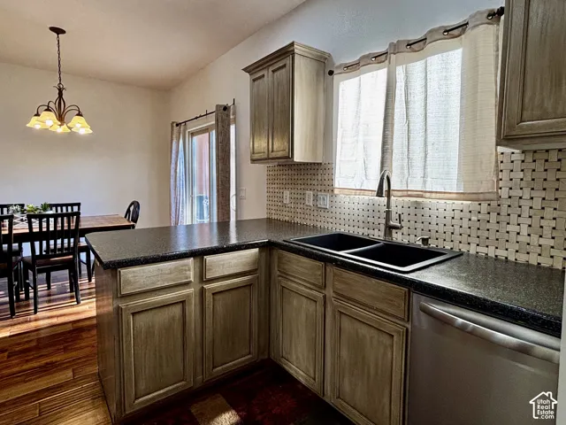 Kitchen featuring wood-finish cabinetry, dark countertops, a double basin sink, and a stainless steel dishwasher