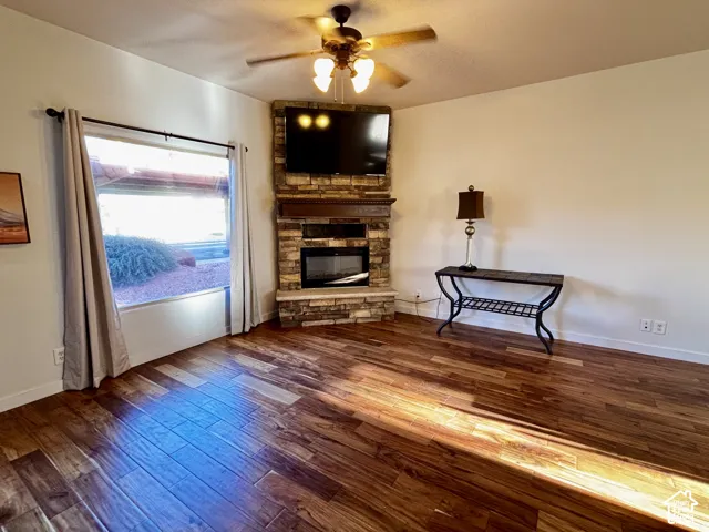 Wood flooring throughout, corner-mounted stone-clad fireplace, integrated mantel, and ceiling fan with light fixture