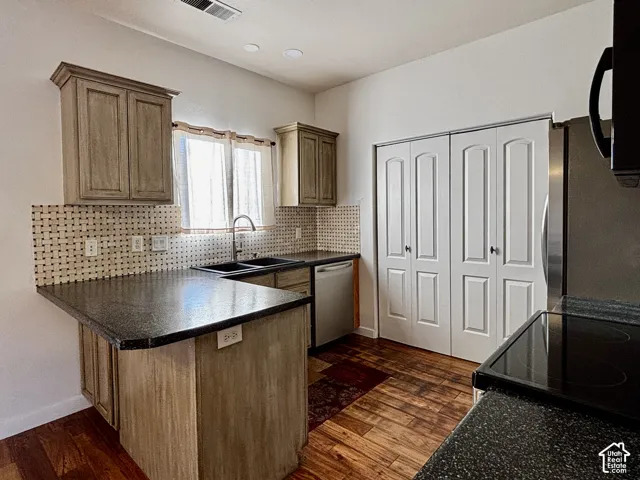Kitchen featuring wood flooring, dark speckled countertops, light wood-finish cabinetry, a stainless-steel refrigerator, and a stainless-steel dishwasher